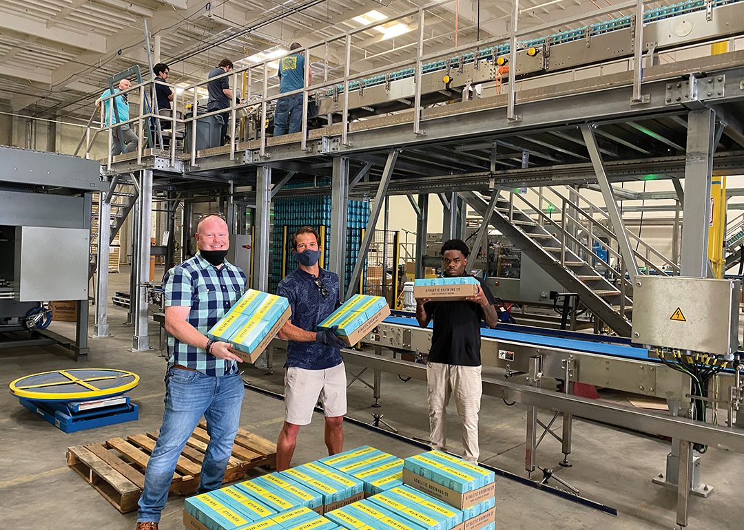 Athletic Brewing workers holding cases of beer in warehouse