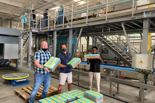 Athletic Brewing workers holding cases of beer in warehouse