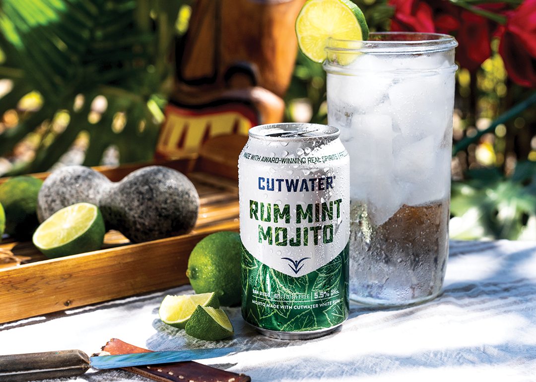 Rum Mint Mojito CutWater Spirits can posed with an ice cold drink, limes, and a garden tiki backdrop