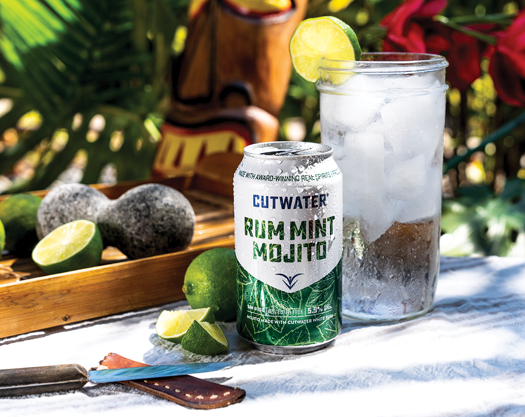 Rum Mint Mojito CutWater Spirits can posed with an ice cold drink, limes, and a garden tiki backdrop