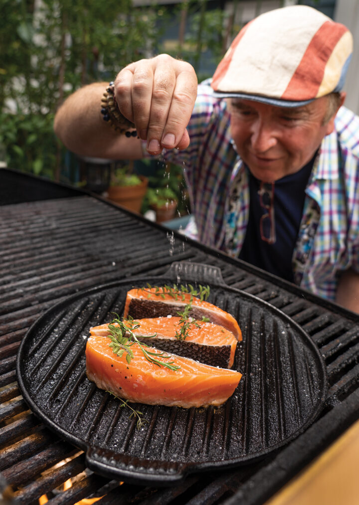 Chef Bernard Guillas salting raw salmon on the grill
