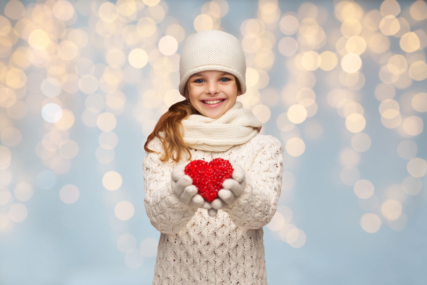 people, christmas, holidays, charity and love concept - smiling teenage girl in winter clothes with small red heart over lights background