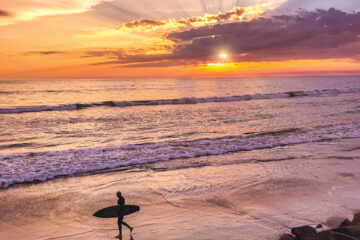 Silhouette of a surfer walking on the beach with a beautiful sunset on the water behind him