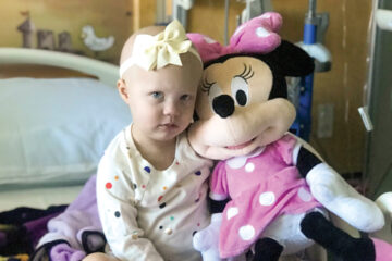 Sick child in hospital bed holding Minnie Mouse stuffed animal
