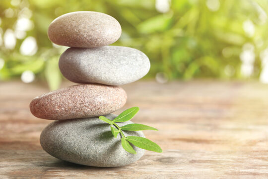Spa stones and bamboo leaves on table against blurred background, space for text. Zen, balance, harmony