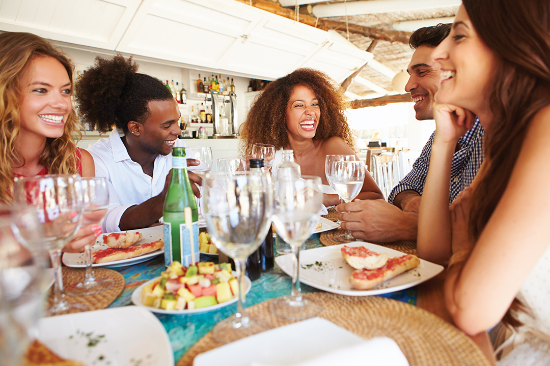 Group Of Young Friends Enjoying Meal In Outdoor Restaurant Smiling