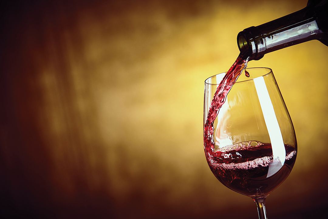 Pouring a single glass of red wine from a bottle in a close up view on the glass over an abstract brown background with copy space