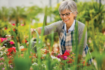 Beautiful older woman in a garden watering flowers