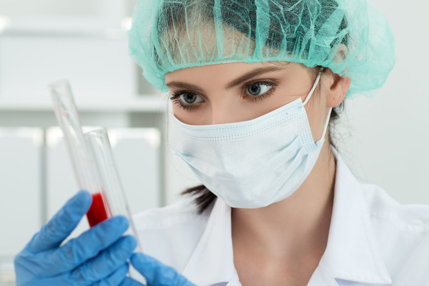 medical doctor in protective gloves and surgical mask and hat comparing two flasks with dark red liquid in laboratory. scientific research, healthcare and medical concept.