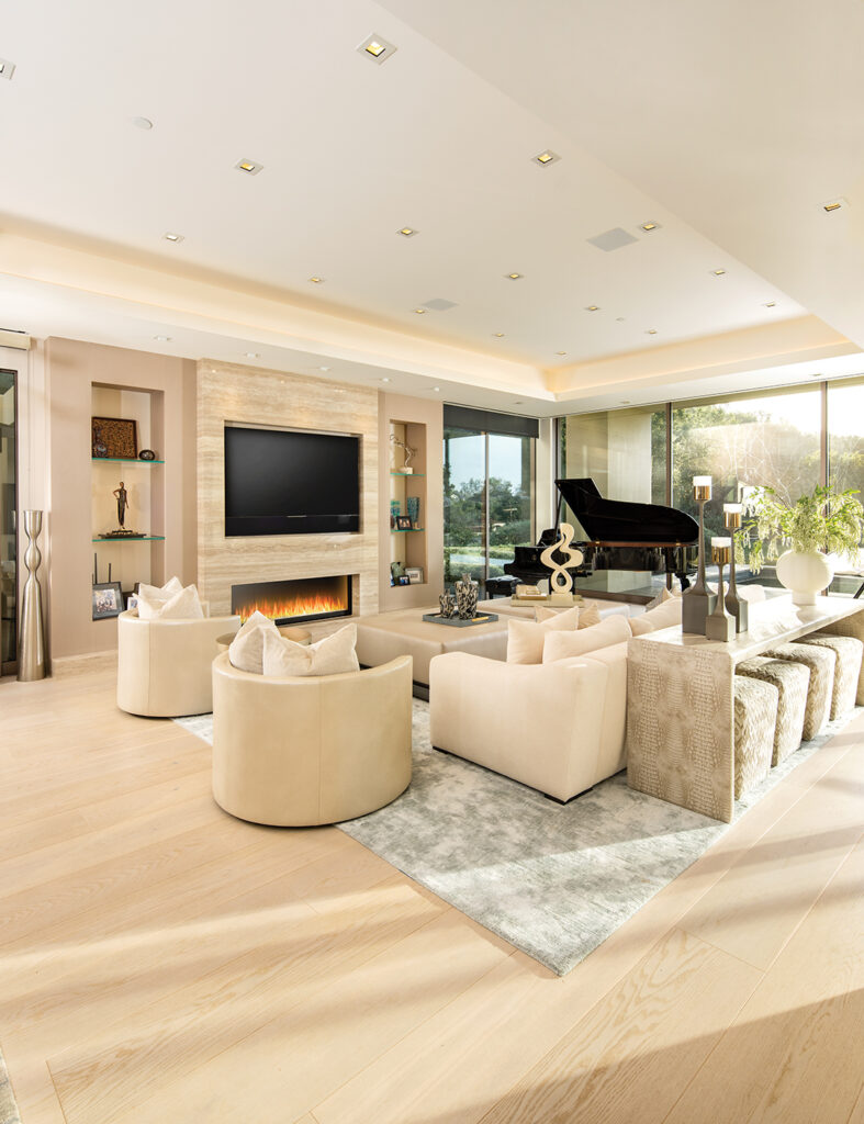 The living room, designed in soothing neutral shades, includes an oversized sofa from Nathan Anthony, leather-and-fabric swivel chairs by Rene Cazares in Los Angeles, and a custom-made, leather-wrapped cocktail table from Le Dimora. The fireplace and television are set into a quartz surround