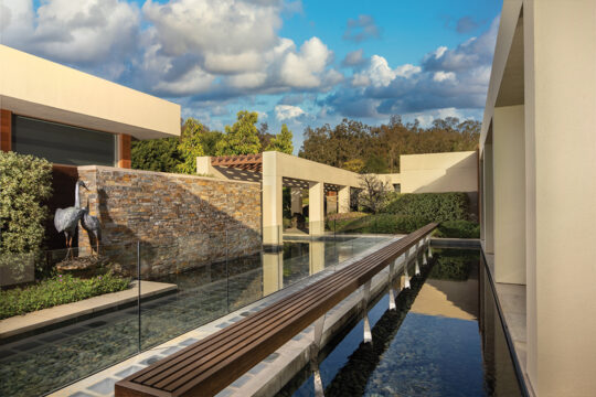 The pergola, reflecting pools, and a pedestrian bridge leading to the entrance “provide a transition from exterior to interior and visually connect the residence to its site,” says architect Robert Griffin