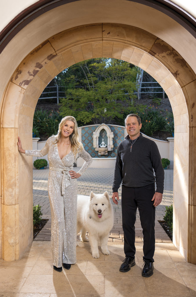 Stacy and Tom McCarthy at the entryway of their Rancho Santa Fe estate. Behind them is a fountain made from a 16th century limestone baptismal font. Yoga sculptures represent serenity and tranquility