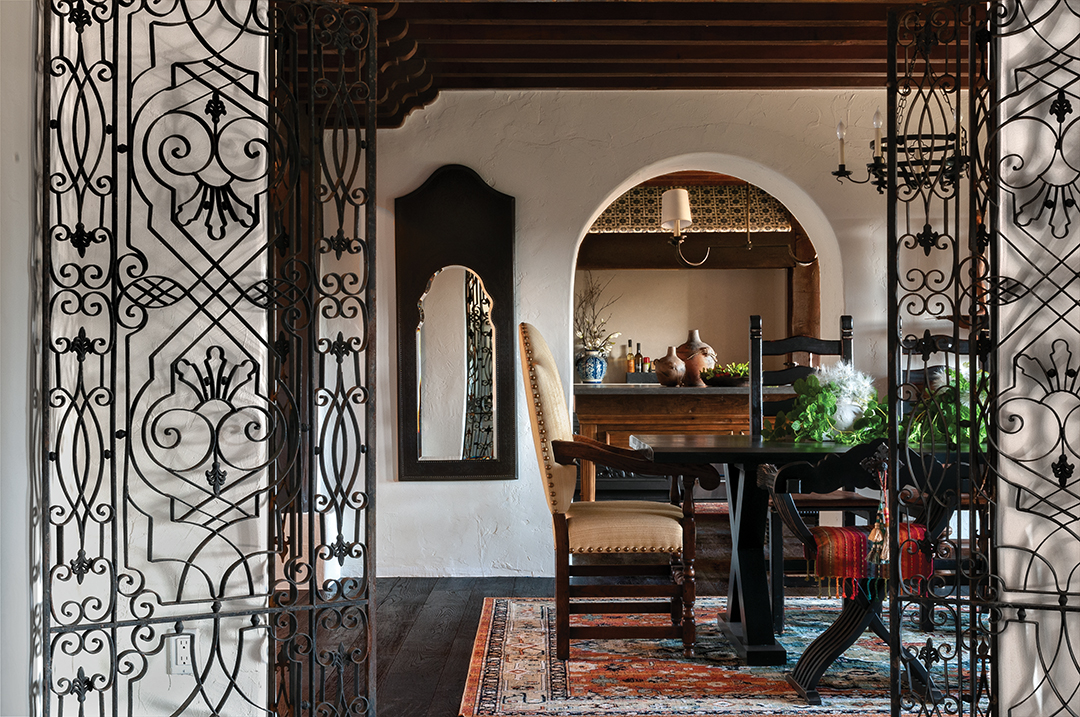 Iron gates in the library open to the dining room with its exposed beams and an embossed, metal-framed mirror