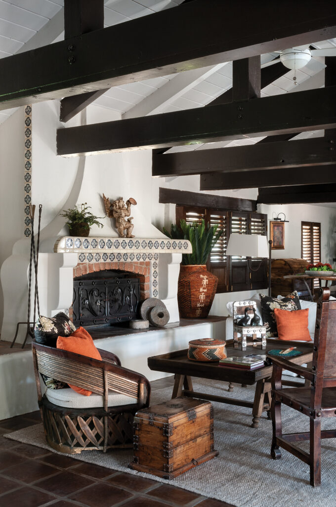 The living room features an open beam ceiling, a plaster and hand-painted tile fireplace, Mexican accent chairs, and a blend of indigenous Mexican and Spanish accessories. The window shutters were handmade in Mexico