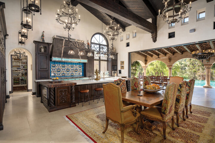 The expansive kitchen and great room features a vaulted ceiling, hand-honed beams, custom lighting, hand-carved cabinetry, hand- painted tiles, and Turkish marble flooring