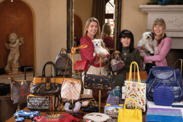 An “angel” hovers over “Heavenly Handbags,” a large collection of designer handbags donated by late philanthropists to the FACE Foundation’s Bags & Baubles fundraiser to help sick and injured animals. Pictured are FACE Executive Director Stash McCullough, Founder Cini Robb, and Event Coordinator Sheryl Lynn, with their furry friends