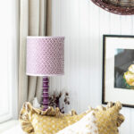 The office features a sofa bed from West Elm, pillows from The Shop Granite Bay, a coffee table from Juxtaposition Home, a desk lamp by Schoolhouse, and a purple lamp from Magnolia Mews with a custom lampshade by Lamp Shades Unlimited