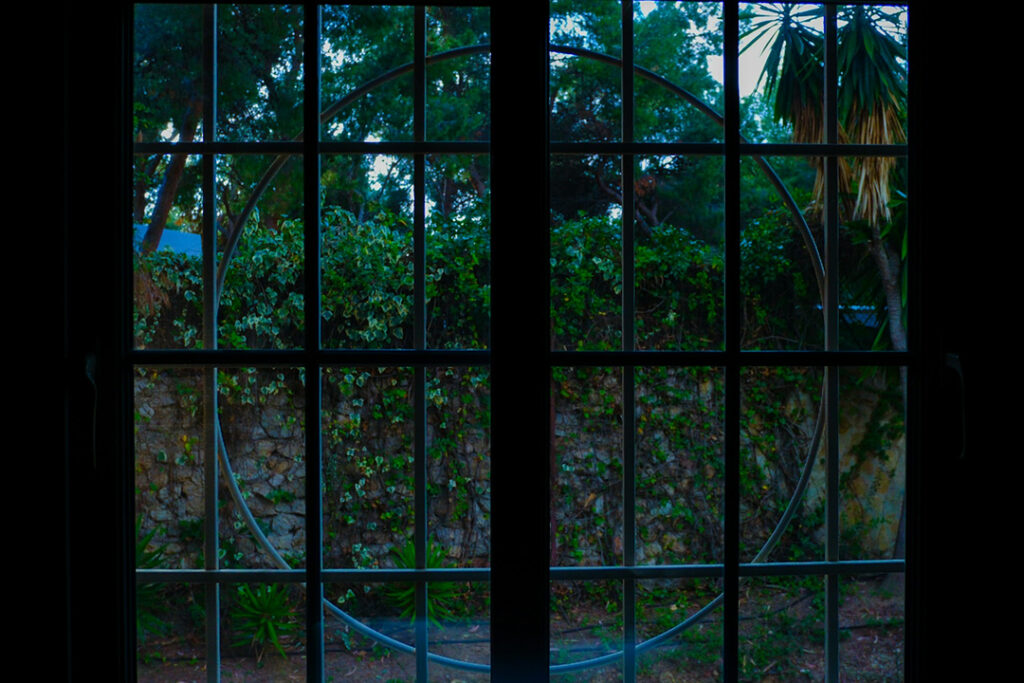 Dark moody photo from inside the house looking out of a round window