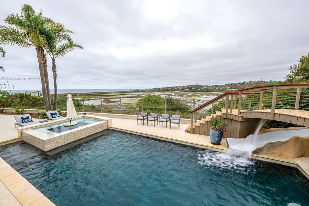 The backyard boasts a spa centered with a table and seating, a swimming pool, waterfall and slide, a bar, and a pickleball/basketball court