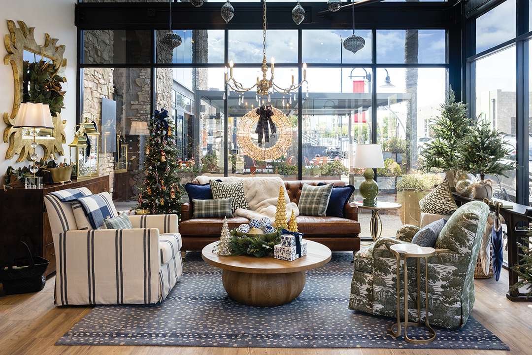 Lounge in the living room on the Maggie leather sofa in tobacco, the Suzanne Kasler Mathes club swivel glider in roper blue, and the Annahelen swivel glider in Sunbrella’s villa green. A bowl of ornaments and trees that light up adorn the Winnona coffee table. Bunny Williams’ Norfolk mirror hangs above the Maxine six-drawer dresser