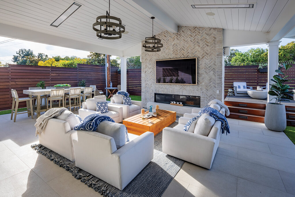 The covered patio features comfortable couches surrounding the outdoor fireplace, a television, and dining areas