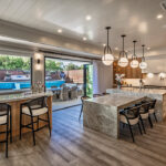 The kitchen, which opens onto the patio, features white oak cabinetry, marble counters, a quartzite dining area, and bar