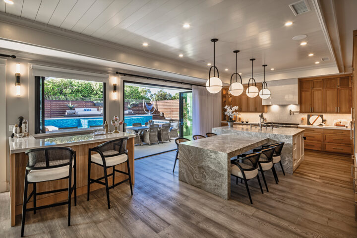 The kitchen, which opens onto the patio, features white oak cabinetry, marble counters, a quartzite dining area, and bar