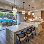 The kitchen, which opens onto the patio, features white oak cabinetry, marble counters, a quartzite dining area, and bar