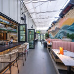 Mia’s beachy vibes extend into an alley lined with coral banquettes care of a wall-length mural of a wave in motion beneath a citrus-hued sunset from local artist Carolina Arrieta