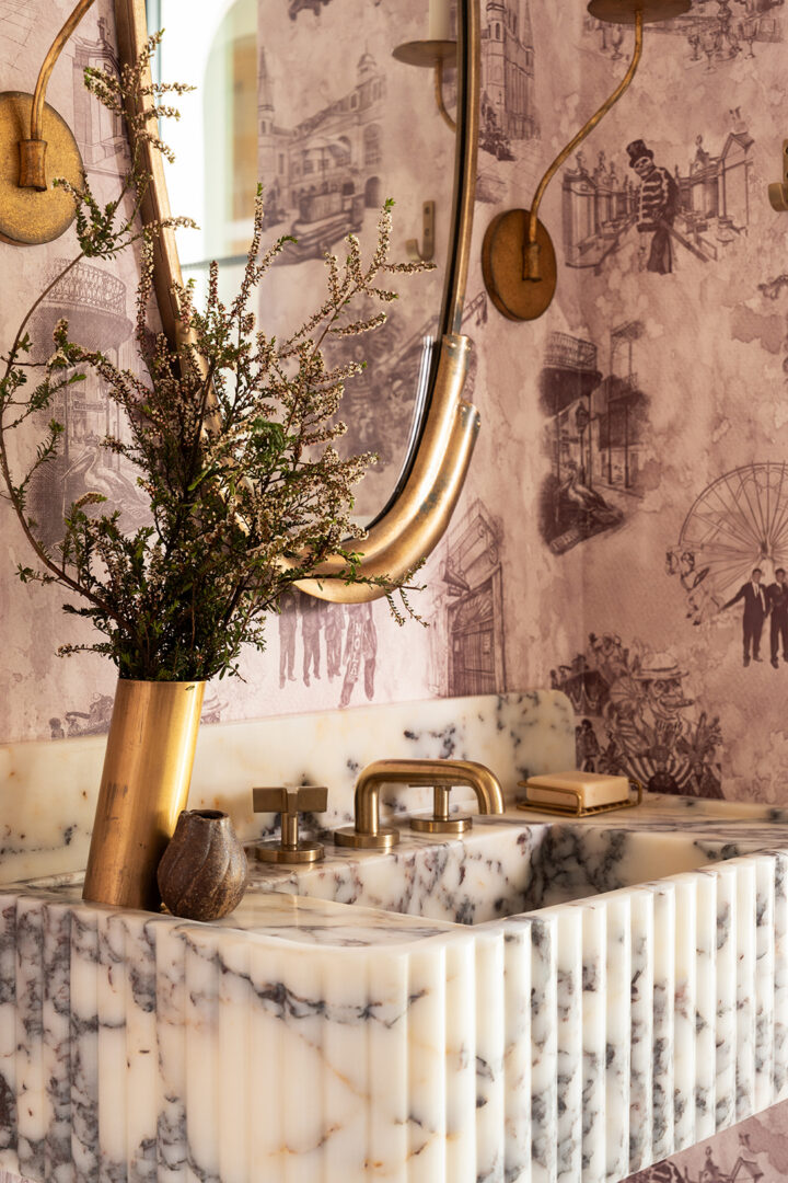 The house reveals itself through moments of personality rather than spectacle. In Garrison’s playbook, bathrooms are the main event. A powder room wrapped in custom New Orleans toile wallpaper is a personal nod to the homeowner’s time there