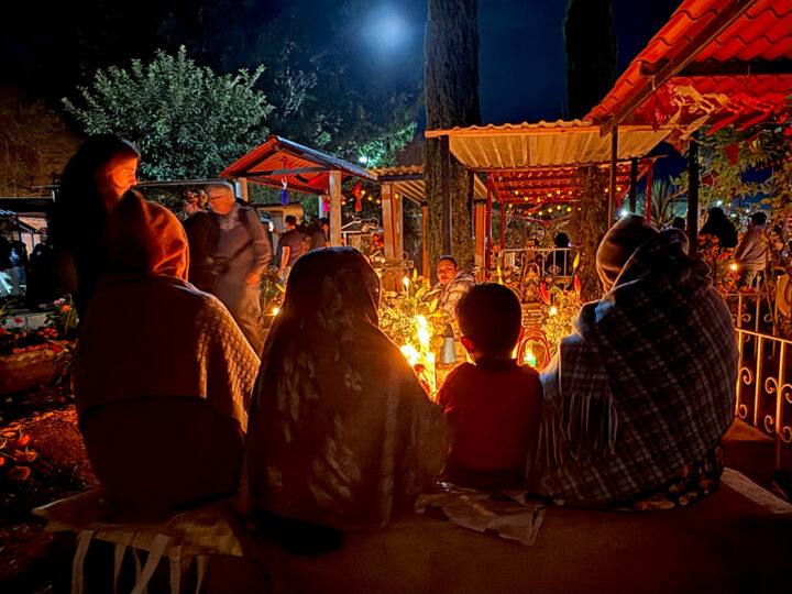 A family sits together at the gravesite of their recently departed relative, honoring them with candles and flowers